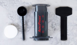 Badger & Dodo. The Aeropress Starter Kit includes filter papers, scoop, chamber, plunger, and stirrer—everything you need to brew delicious coffee. Shown on a white surface.
