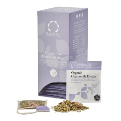 Badger and Dodo Coffee Roasters: The Organic Chamomile Dream box from Solaris Tea, elegantly purple and containing individual sachets, is showcased with a tea bag and loose organic chamomile leaves artfully displayed in front of it.
