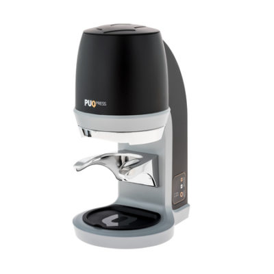 Badger and Dodo Coffee Roasters: The Puqpress Q2 is a stylish espresso tamper with a modern black and silver design, featuring a curved handle and digital side display, mounted on a light-colored base.
