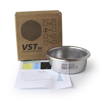 Badger and Dodo Coffee Roasters: A stainless steel VST precision filter basket is shown next to its cardboard box packaging. A data sheet with graphs and information is placed underneath the filter basket, partially visible in the image.