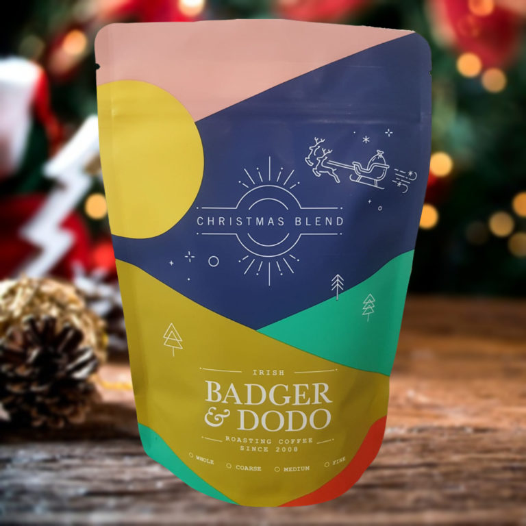 Badger and Dodo Coffee Roasters: The festive Christmas Blend coffee package from Badger & Dodo features a vibrant design with a sleigh, reindeer, and a backdrop of twinkling Christmas lights and pinecone accents.