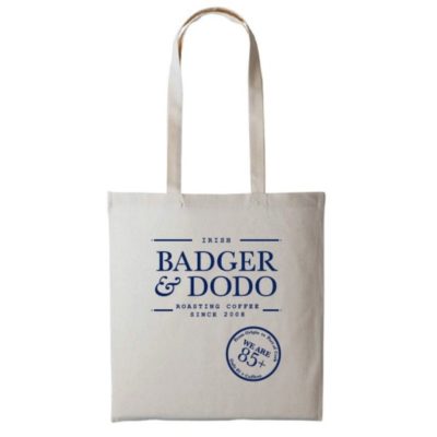 Badger and Dodo Coffee Roasters: The Badger and Dodo Tote Bag (Blue) is a stylish beige accessory with Irish Badger & Dodo Roasting Coffee Since 2008 in blue text and We Are 85+ beneath it. With two sturdy handles, its perfect for carrying your essentials.