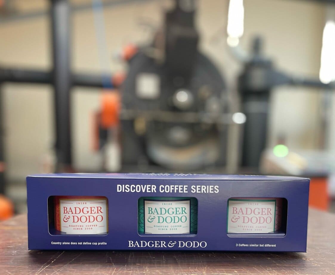 Badger and Dodo Coffee Roasters: The Discover Coffee Series boxed set showcases three exquisite Badger & Dodo coffee packets, all set against a backdrop of blurred industrial coffee roasting equipment, inviting you to explore the art of brewing.