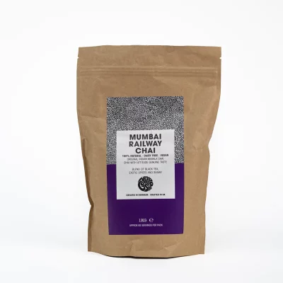 Badger and Dodo Coffee Roasters: On a brown paper bag, labeled Mumbai Railway Chai (1kg), a purple and white label with a black pattern boasts the chais 100% natural, vegan, and sugar-free qualities. Filled with exotic spices, it promises an authentic chai experience.