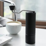 Badger & Dodo. A Timemore Grinder Chestnut espresso and a cup of coffee rest on a white table by a sunlit window.