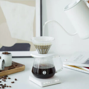 Badger & Dodo. A hand pours water from a gooseneck kettle over a coffee dripper, precisely brewing coffee on the Mirror Nano White - Timemore digital scale.