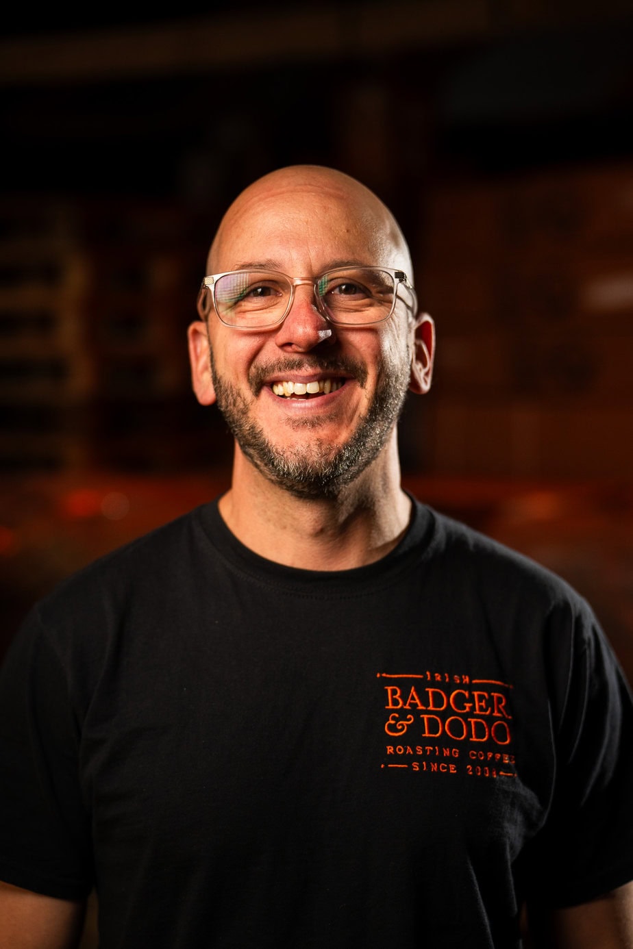 Badger & Dodo. Meet The Team: Smiling man with glasses and a beard wearing a black Badger & Dodo Roasting Coffee t-shirt.