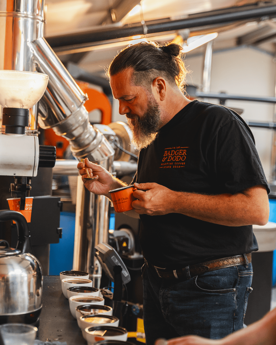 Badger & Dodo. Man tasting coffee samples in a modern coffee roastery, holding a spoon and an orange cup—perfectly capturing the experience offered to every wholesale partner.