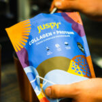 Badger & Dodo. Someone holds a Juspy Collagen+Protein Powder-400g pouch, showcasing its protein-packed cacao superfood benefits.