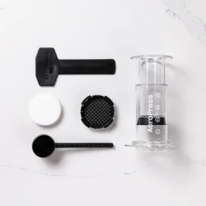Badger & Dodo. The Aeropress Coffee Maker-Clear Colours kit is disassembled, showing its filter, scoop, stirrer, and cap in transparent hues on a white surface.
