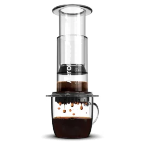 Badger & Dodo. The Aeropress Coffee Maker-Clear Colours presses rich, dark coffee into a glass mug, with vibrant colors highlighting each drip below.