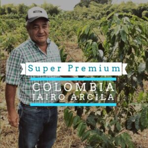 A man wearing a cap and plaid shirt stands in a coffee farm surrounded by green coffee plants. Overlaid text reads “Super Premium Colombia Jairo Arcila.”